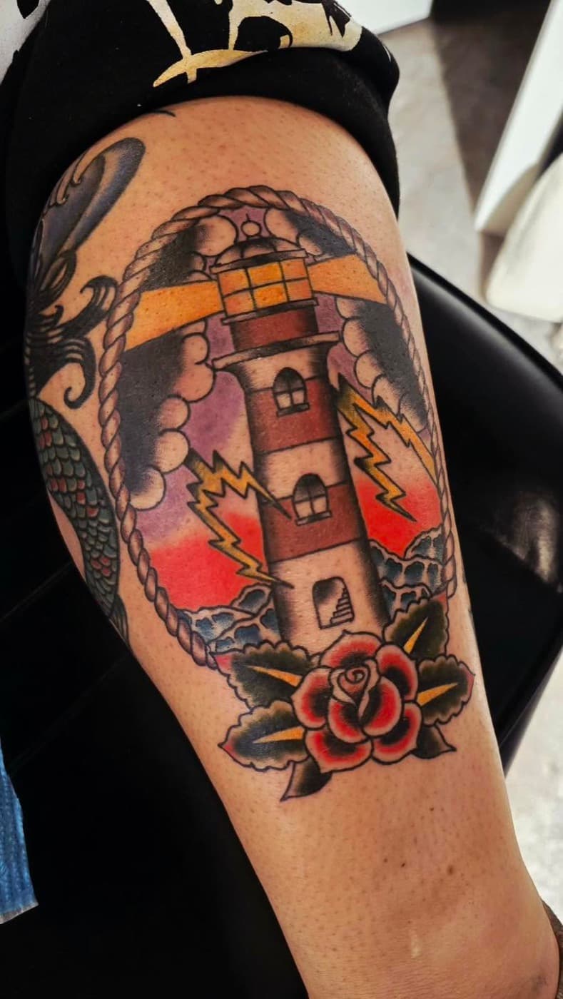 Traditional lighthouse inside a rope frame, lightning either side and a rose at its base