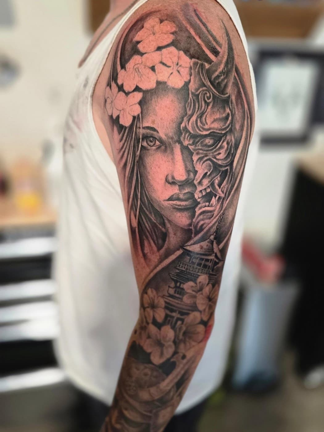 A woman’s face split with a hannya mask, cherry blossoms and a pagoda below, upper arm