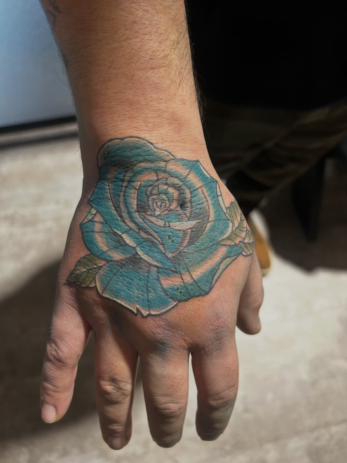 Teal rose with green leaves covering the back of the hand