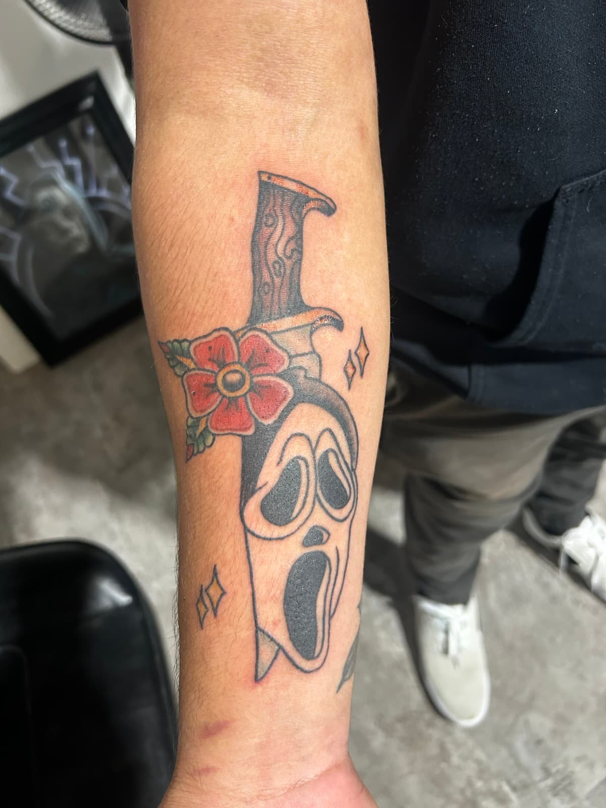 Ghostface mask pierced by a dagger with a red flower, colour on the forearm