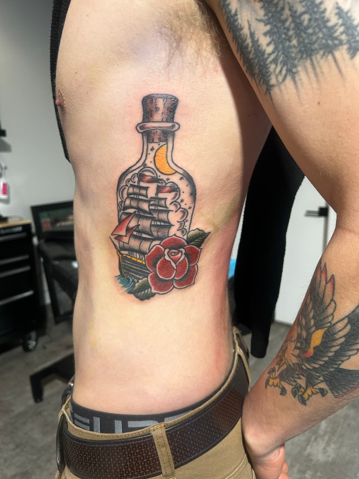 Tall ship in a bottle under a crescent moon, with a red rose, colour on the ribs