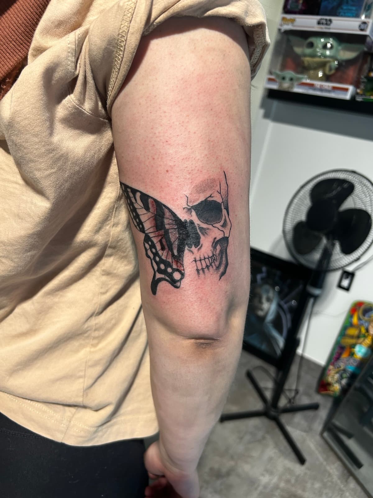 Half skull joined to half a butterfly wing, black on the back of the arm
