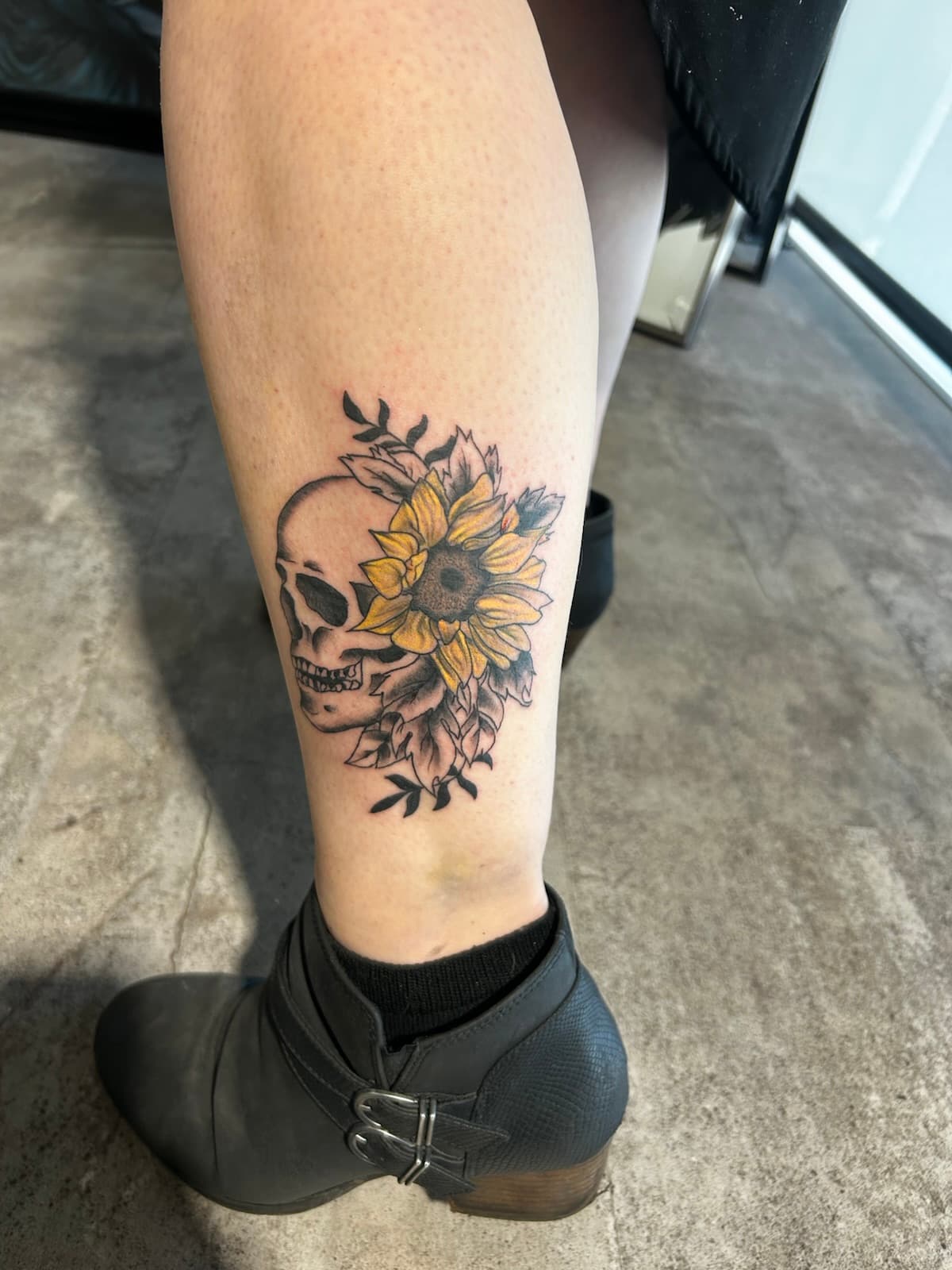 Skull half hidden behind a yellow sunflower and leaves, on the calf