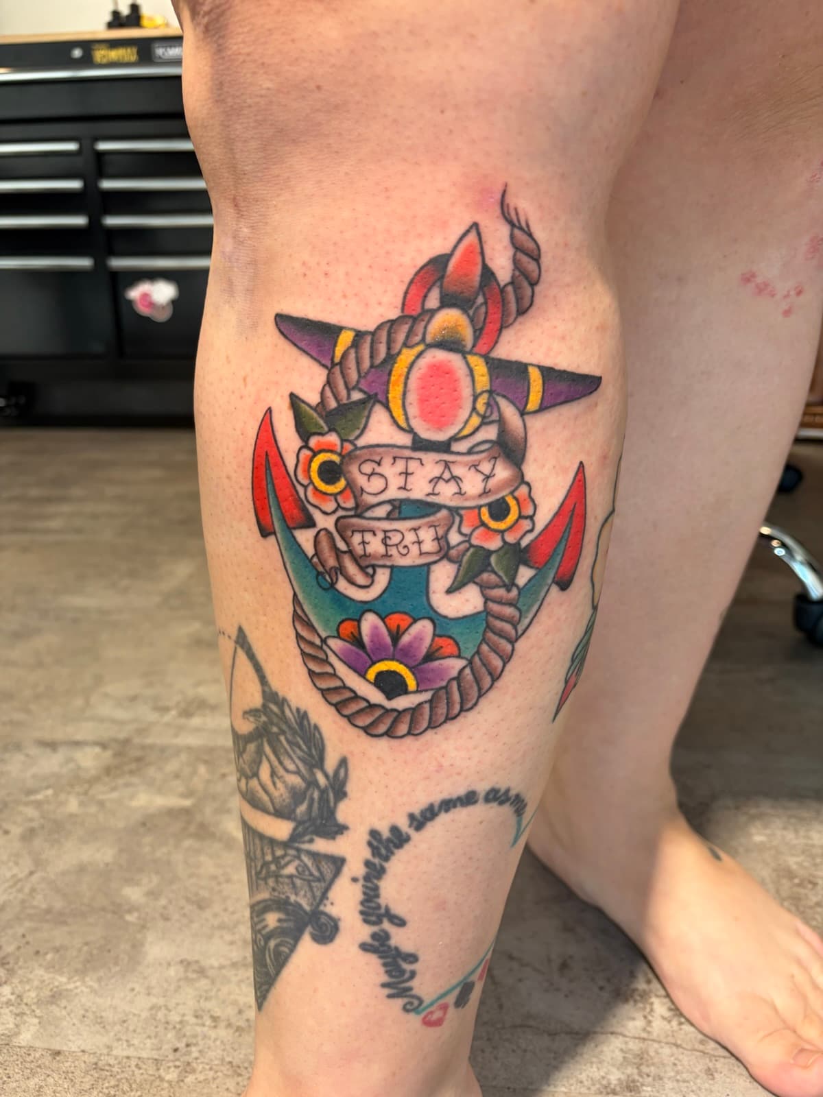 Rope-wrapped anchor with flowers and a 'Stay True' banner, colour on the calf