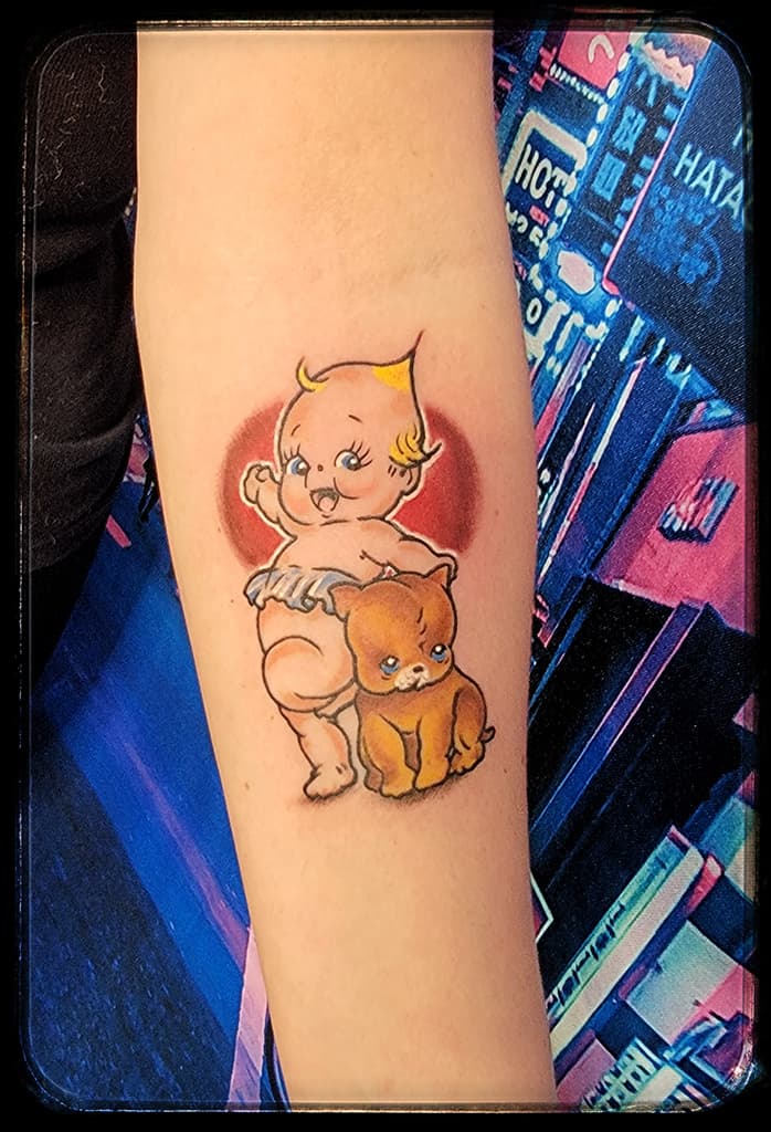 Kewpie baby in a nappy beside a brown puppy, colour on the inner forearm