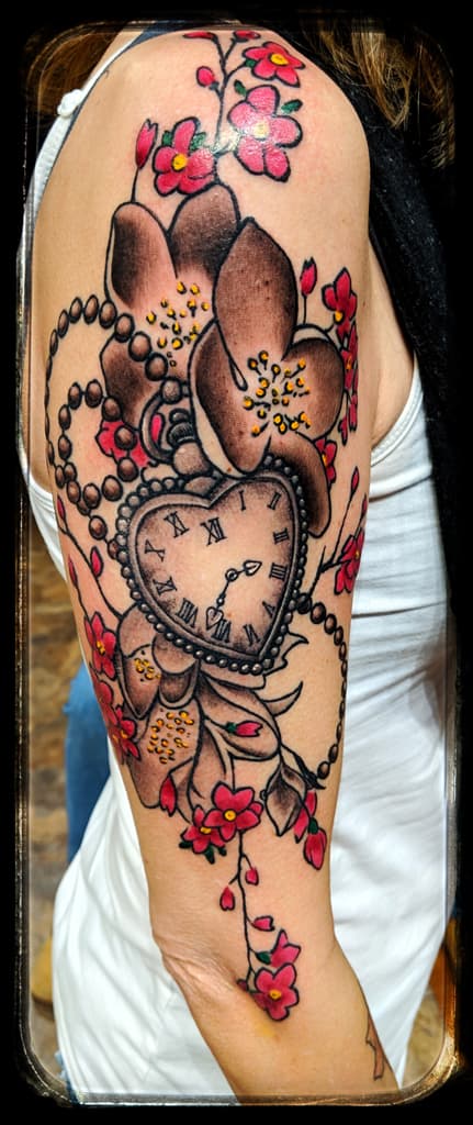 Heart-shaped clock among brown orchids, pink cherry blossoms and pearl strands, colour half sleeve on the upper arm
