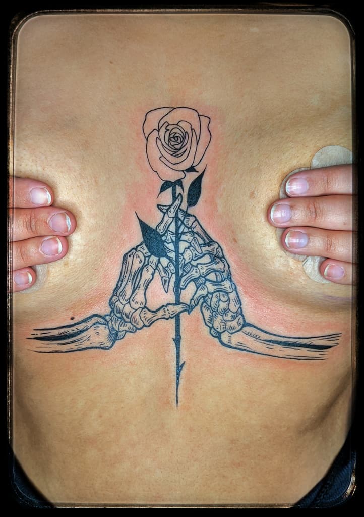 Skeleton hands holding a long-stemmed rose, black linework on the sternum below the chest