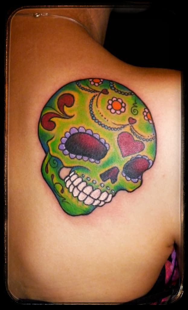 Green sugar skull with a pink heart, flowers and purple eye rims, colour on the shoulder blade