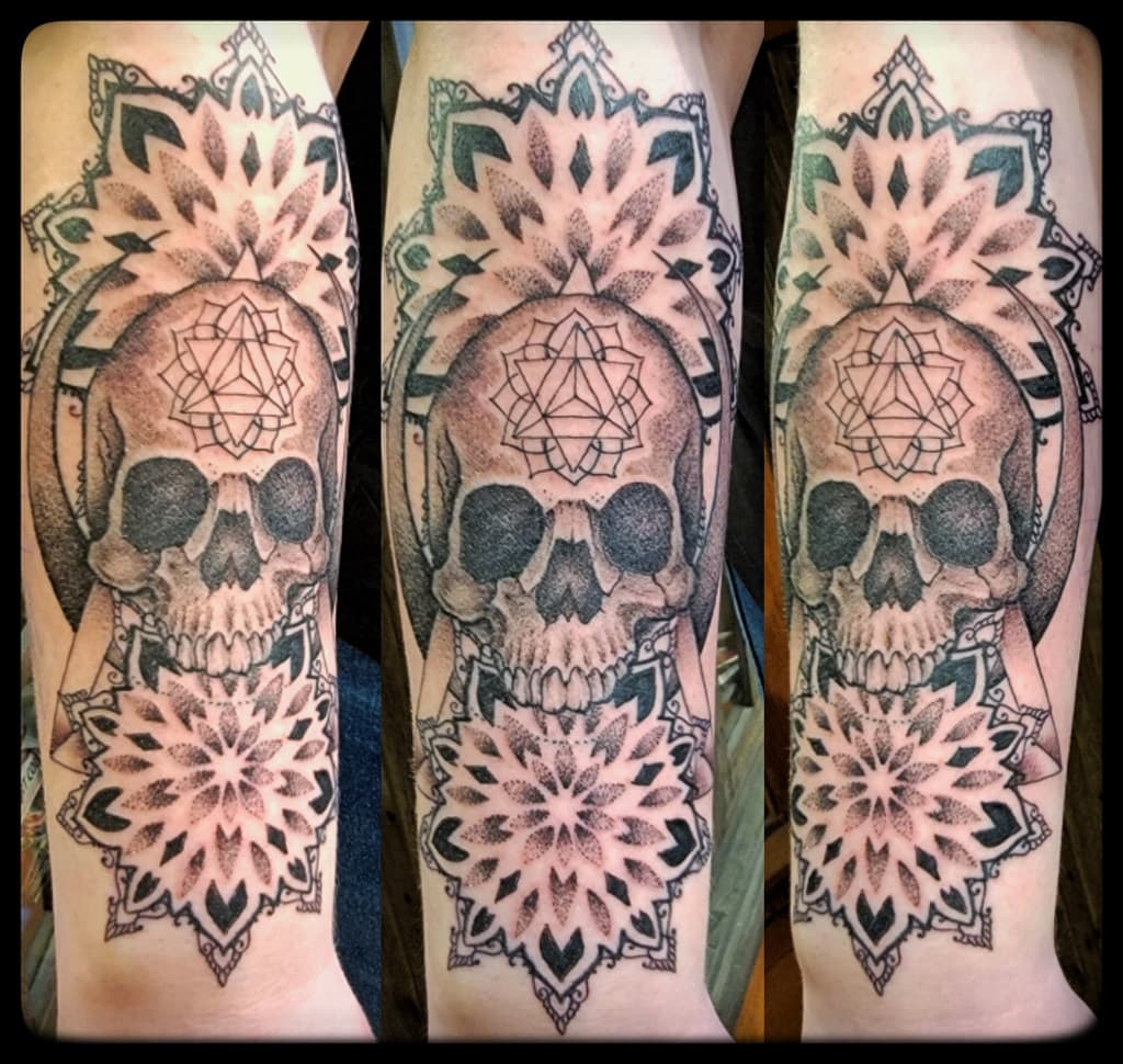 Human skull with a geometric triangle on the forehead framed by dotwork mandalas, black and grey forearm, three angles
