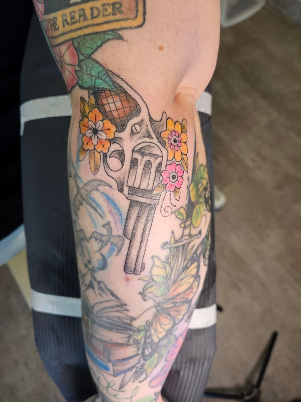 Revolver among orange and pink daisies, neo traditional colour on the leg