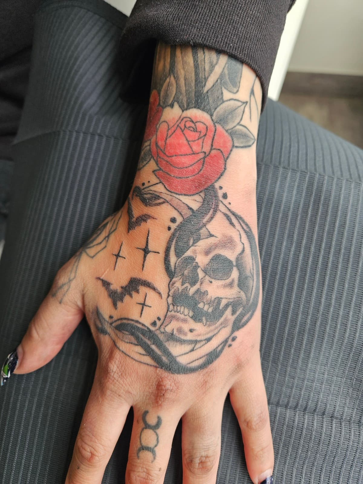 Skull under a red rose with bats and four-point stars, on the back of the hand