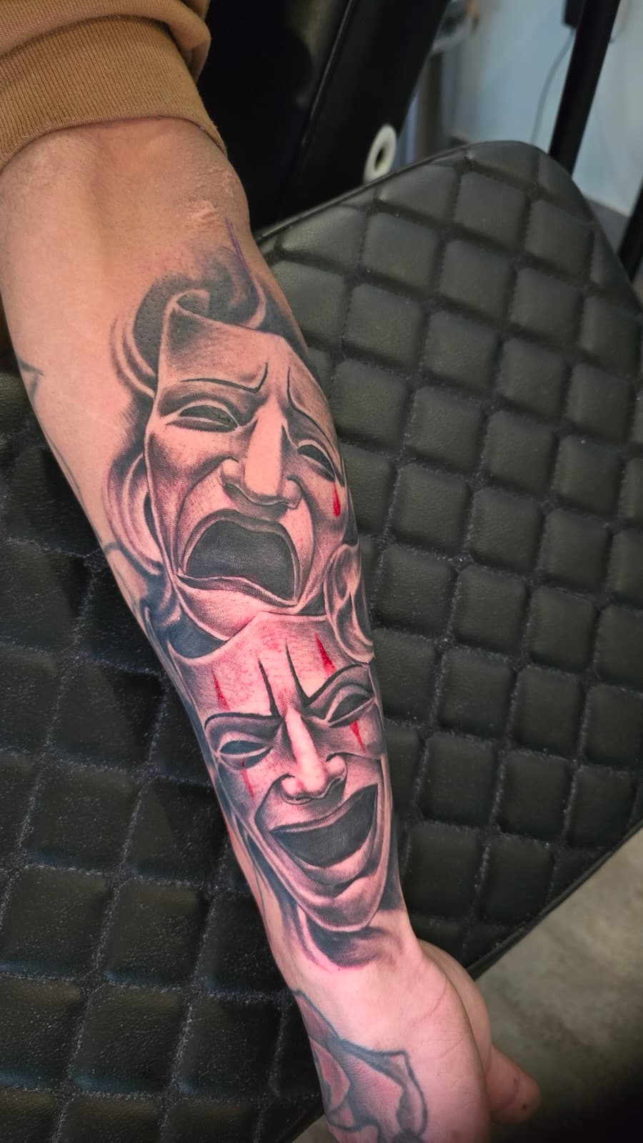Comedy and tragedy theatre masks stacked down the forearm, black and grey with red tears