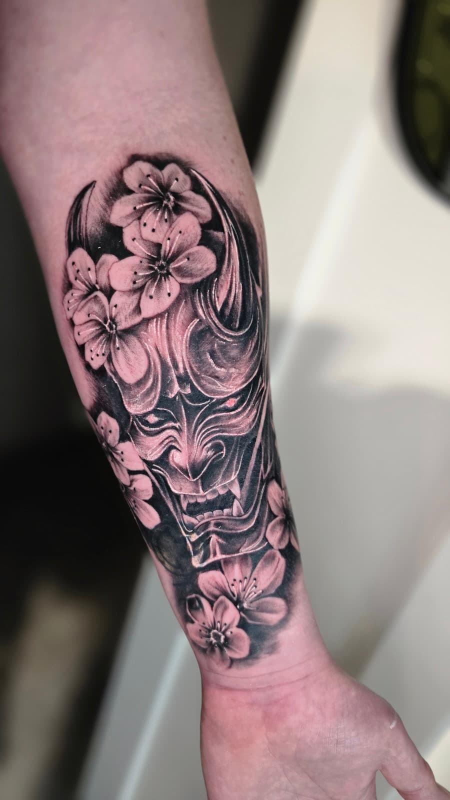 Hannya mask framed by cherry blossoms, black and grey on the forearm