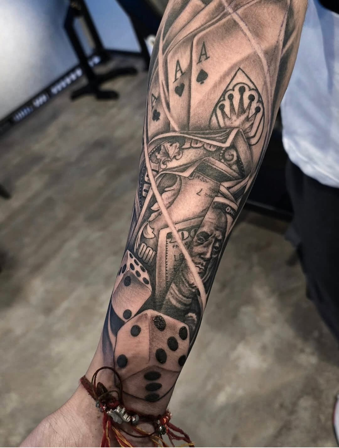 Aces, a king and dice stacked down the forearm, black and grey