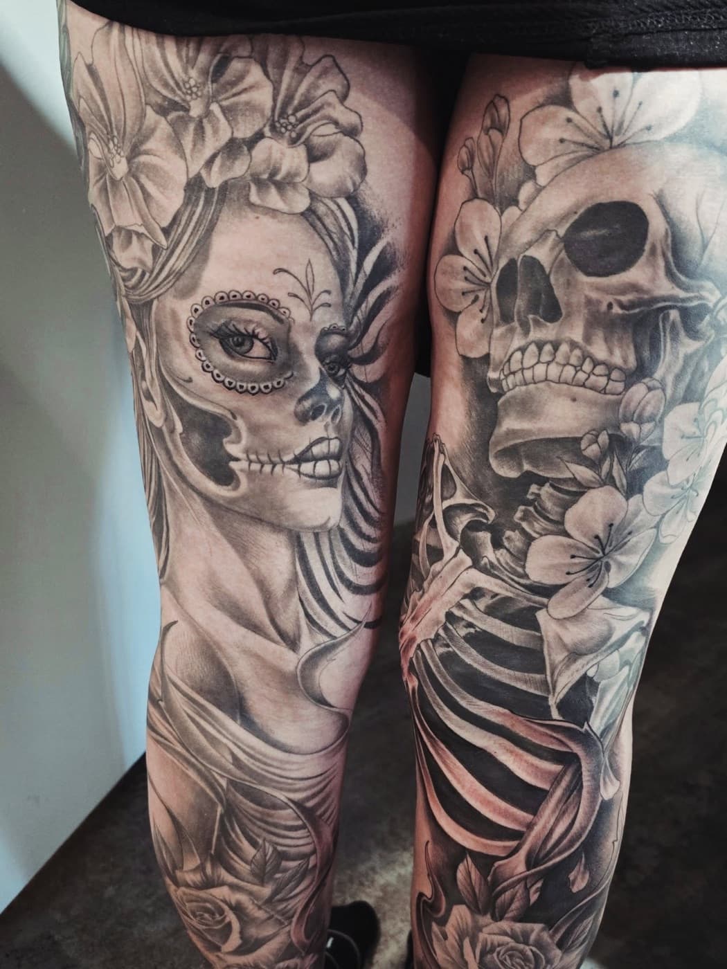 A pair of black and grey leg pieces — a woman in Day of the Dead makeup on one, a skull and skeleton among blossoms on the other